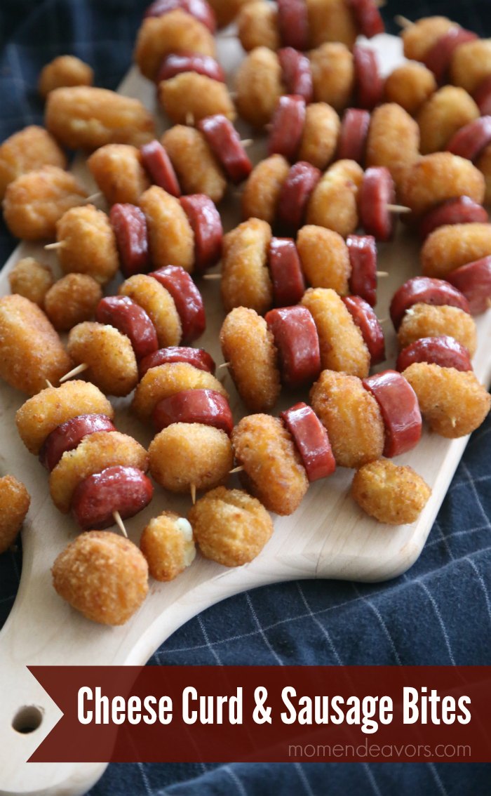 A wooden tray with fried cheese curd and sausage skewers
