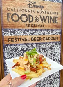 A plate of brisket fries in front of a Disney Food & Wine Festival Sign