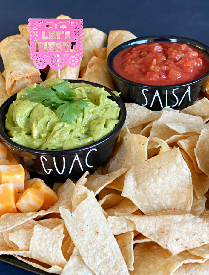 Tortilla chips in foreground with bowls of guacamole and salsa