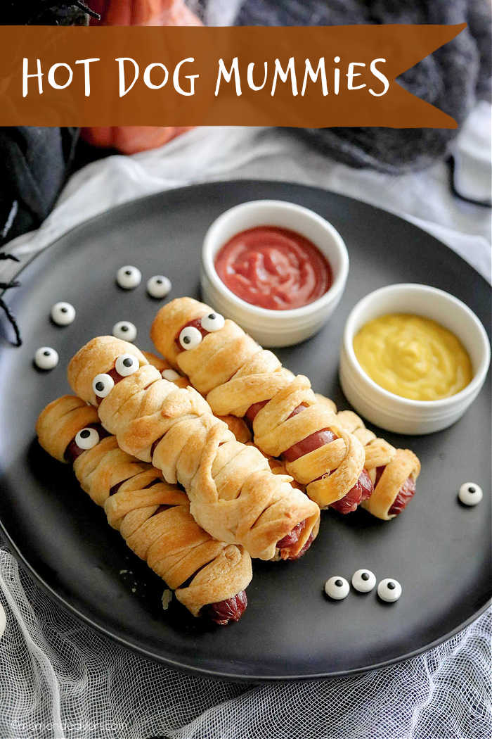 Mummy hot dogs on a plate with dip bowls of ketchup and mustard