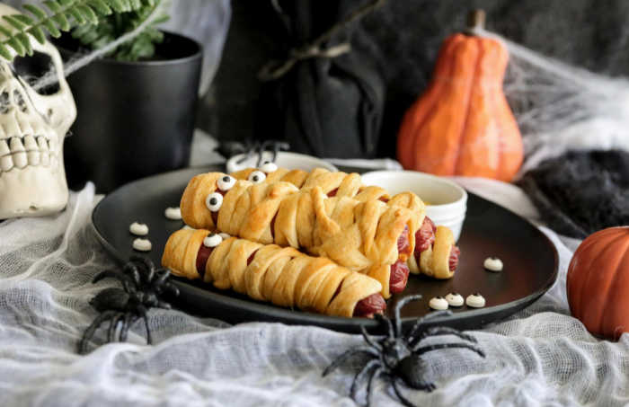 Mummy Hot Dogs on a plate with some Halloween decorations in the background